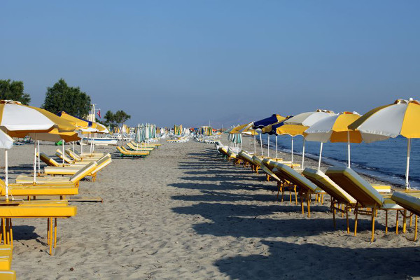 Sonnenschirme und Liegen stehen in Reihen am Strand von Tigáki